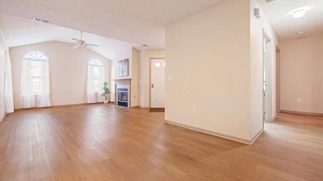 unfurnished living room with vaulted ceiling, a tile fireplace, a textured ceiling, and light hardwood / wood-style flooring