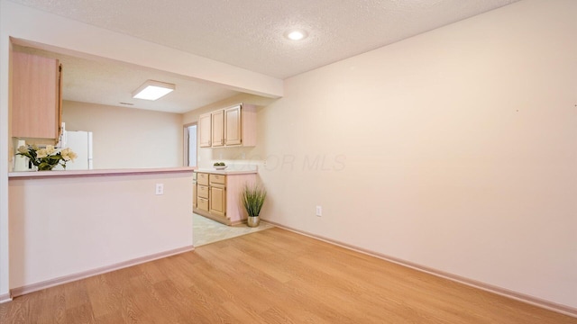 kitchen with kitchen peninsula, light wood-type flooring, light brown cabinets, a textured ceiling, and white refrigerator