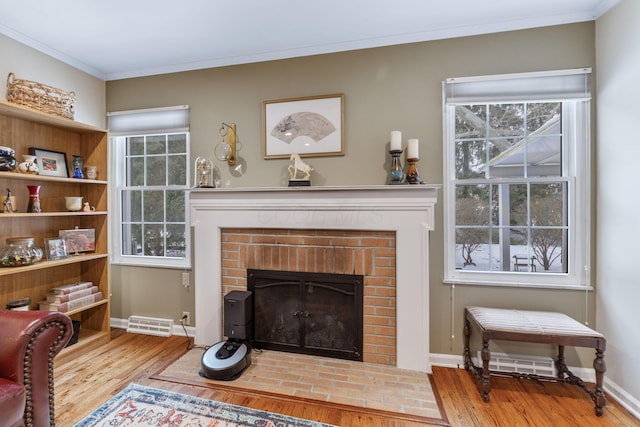 living room with light wood-type flooring, ornamental molding, and a fireplace