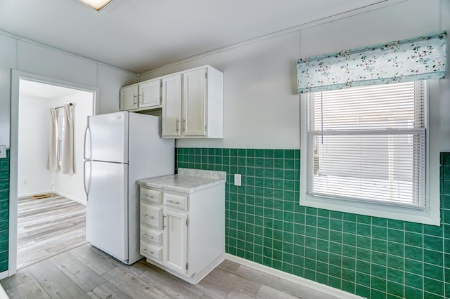 kitchen with light wood-type flooring, tile walls, white refrigerator, and white cabinetry