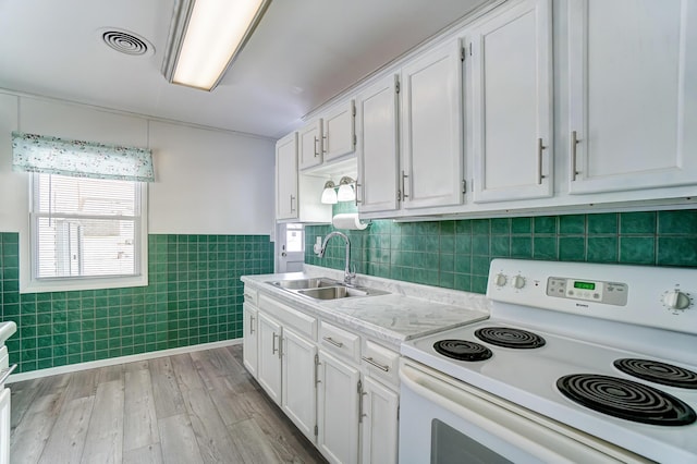 kitchen with electric stove, tile walls, white cabinets, and sink