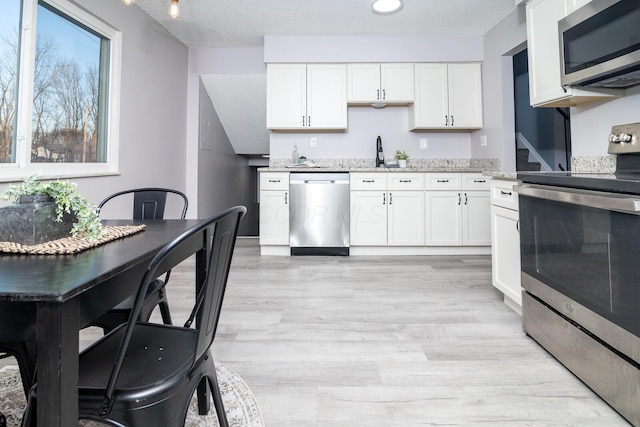 kitchen with stainless steel appliances, white cabinets, light stone counters, and sink