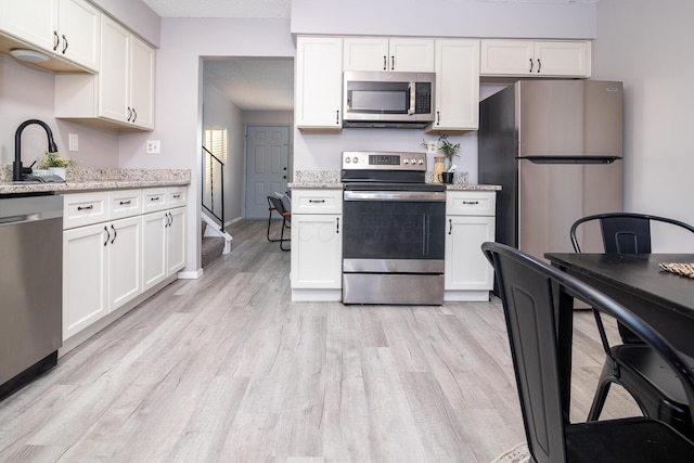 kitchen with white cabinetry, stainless steel appliances, sink, light wood-type flooring, and light stone counters