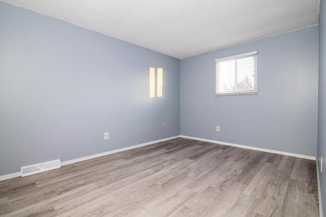 spare room with lofted ceiling, a textured ceiling, and light hardwood / wood-style flooring