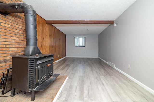 living room featuring light hardwood / wood-style flooring, beamed ceiling, a wood stove, and a textured ceiling