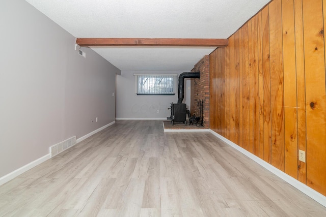 unfurnished living room featuring beam ceiling, wooden walls, a wood stove, and a textured ceiling