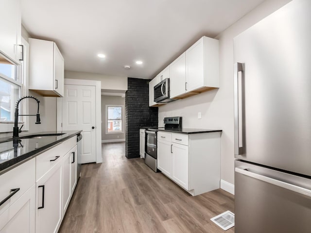 kitchen featuring sink, white cabinetry, dark stone counters, light wood-type flooring, and stainless steel appliances