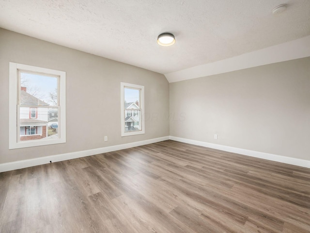 unfurnished room with wood-type flooring, vaulted ceiling, and a textured ceiling