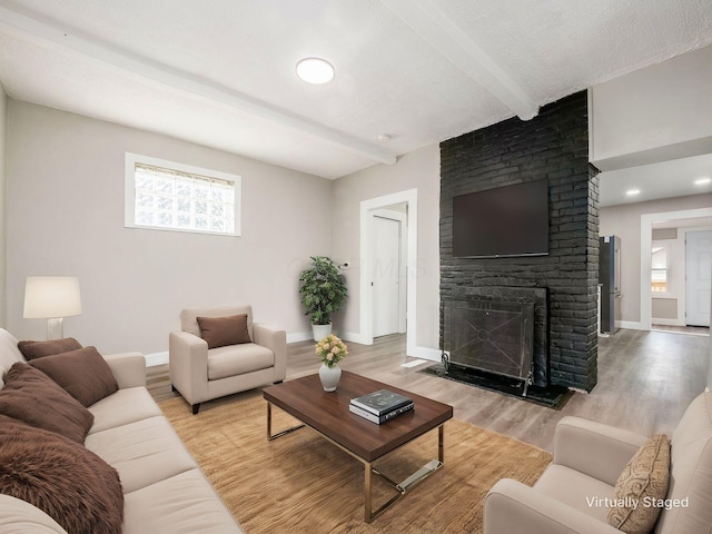 living room featuring beamed ceiling, a fireplace, light hardwood / wood-style floors, and a textured ceiling