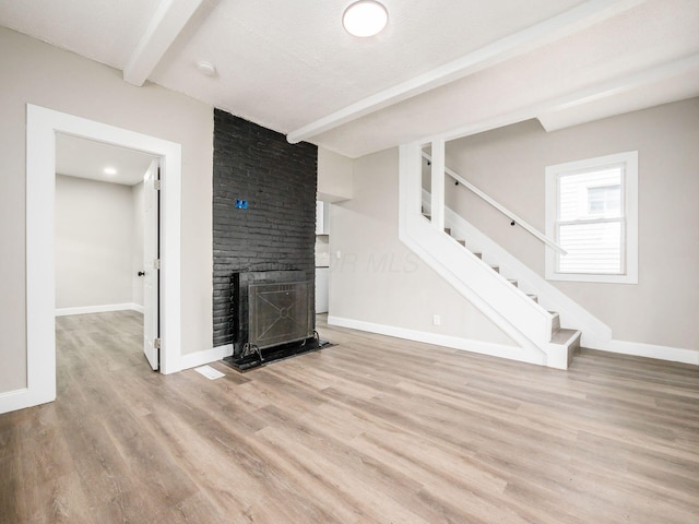 unfurnished living room with a brick fireplace, beam ceiling, and light hardwood / wood-style floors