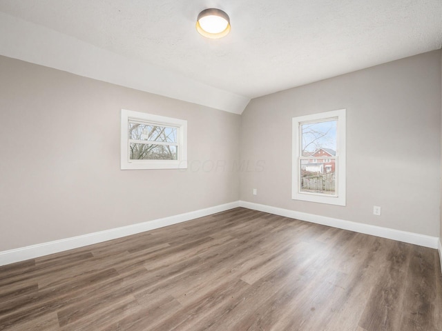 spare room featuring dark hardwood / wood-style flooring, vaulted ceiling, and a textured ceiling