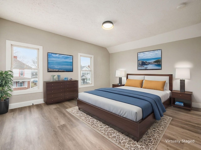 bedroom with vaulted ceiling, hardwood / wood-style floors, and a textured ceiling