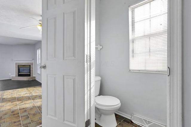 bathroom featuring ceiling fan, a fireplace, toilet, and a textured ceiling