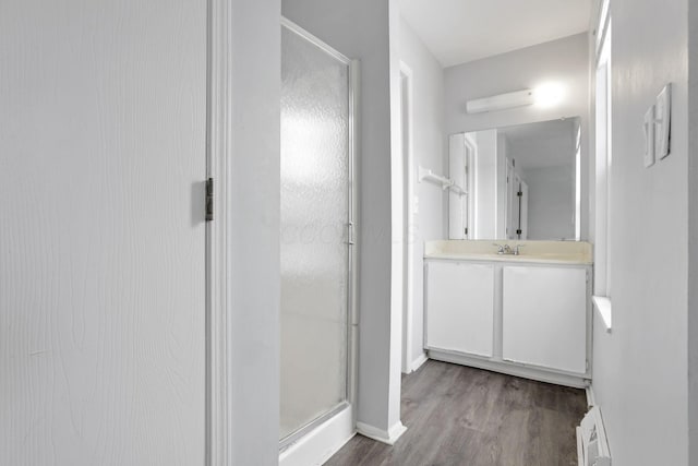 bathroom featuring vanity, baseboard heating, a shower with door, and hardwood / wood-style floors