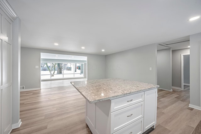 kitchen featuring light hardwood / wood-style flooring, light stone counters, white cabinetry, and a kitchen island