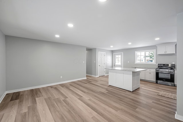 kitchen with light wood-type flooring, a kitchen island, white cabinetry, and stainless steel stove