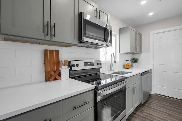 kitchen with sink, gray cabinetry, dark hardwood / wood-style flooring, stainless steel appliances, and decorative backsplash