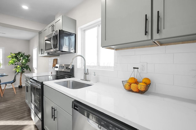 kitchen with appliances with stainless steel finishes, sink, gray cabinetry, backsplash, and light stone countertops