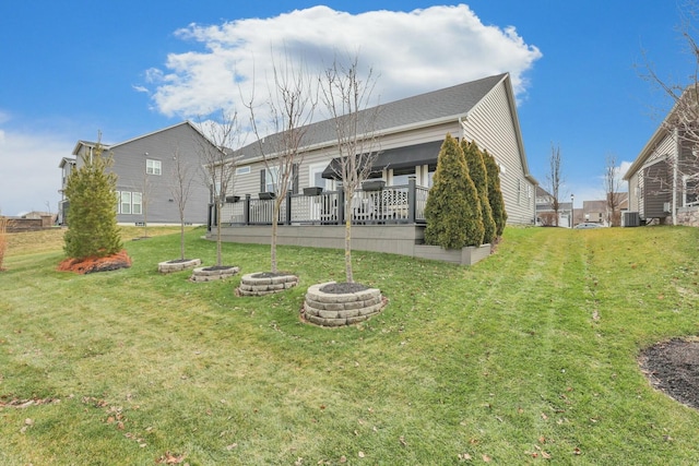 rear view of property featuring a lawn, a deck, central air condition unit, and an outdoor fire pit