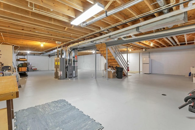 basement featuring white refrigerator, water heater, and heating unit