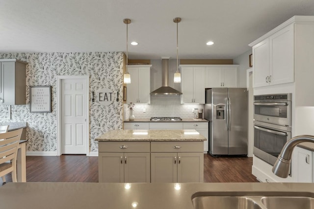 kitchen with pendant lighting, white cabinetry, dark hardwood / wood-style flooring, stainless steel appliances, and wall chimney range hood