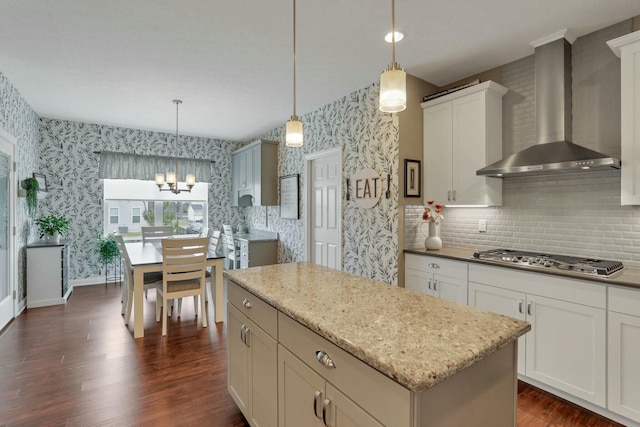 kitchen featuring wall chimney exhaust hood, a center island, stainless steel gas cooktop, and hanging light fixtures