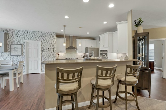 kitchen with decorative light fixtures, white cabinetry, a breakfast bar area, stainless steel appliances, and wall chimney exhaust hood