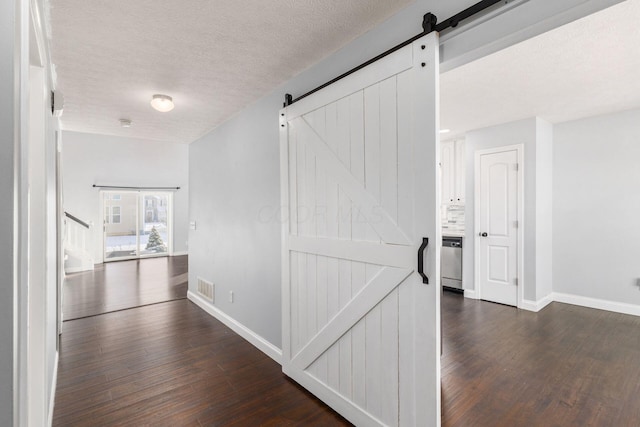 corridor with dark hardwood / wood-style flooring, a barn door, and a textured ceiling