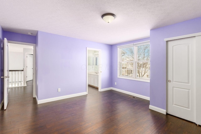 unfurnished bedroom featuring dark hardwood / wood-style flooring, ensuite bath, a closet, and a textured ceiling