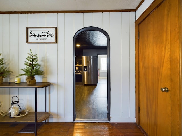 hallway with dark wood-type flooring, wood walls, and ornamental molding