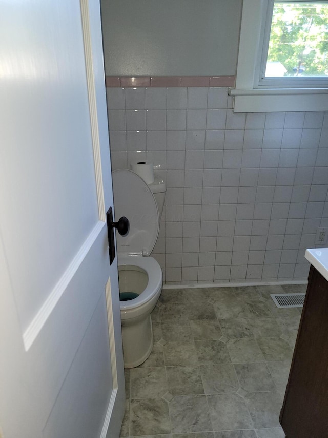 bathroom with vanity, toilet, and tile walls