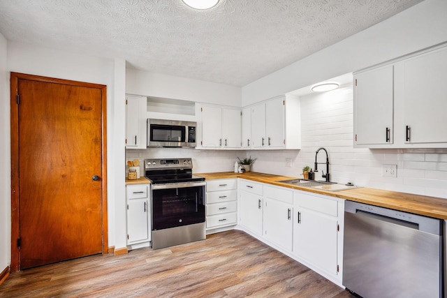 kitchen featuring stainless steel appliances, backsplash, white cabinets, light hardwood / wood-style flooring, and sink