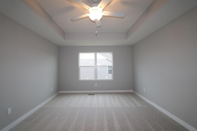 unfurnished room featuring a raised ceiling, light colored carpet, and ceiling fan