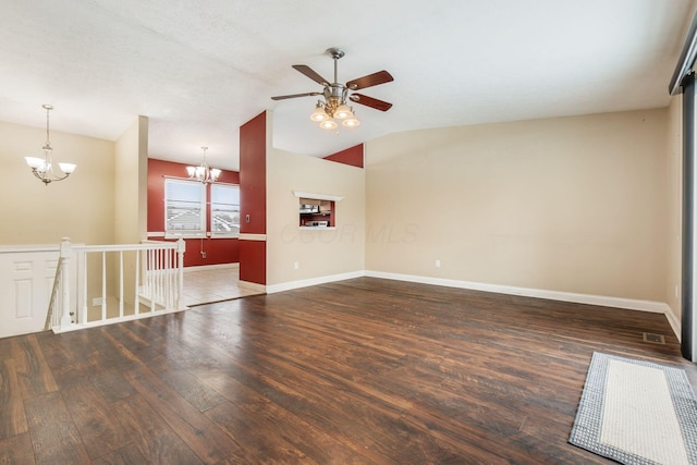 empty room featuring ceiling fan with notable chandelier, dark wood-type flooring, and vaulted ceiling