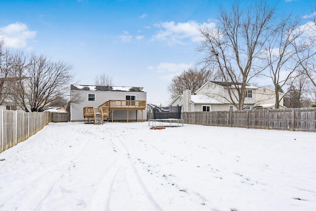 snow covered house featuring a trampoline and a deck