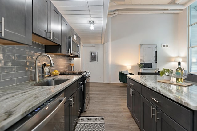 kitchen featuring tasteful backsplash, sink, light stone counters, light hardwood / wood-style floors, and stainless steel appliances