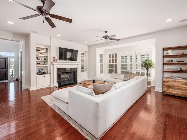 living room with ceiling fan, built in features, a tile fireplace, and dark hardwood / wood-style floors