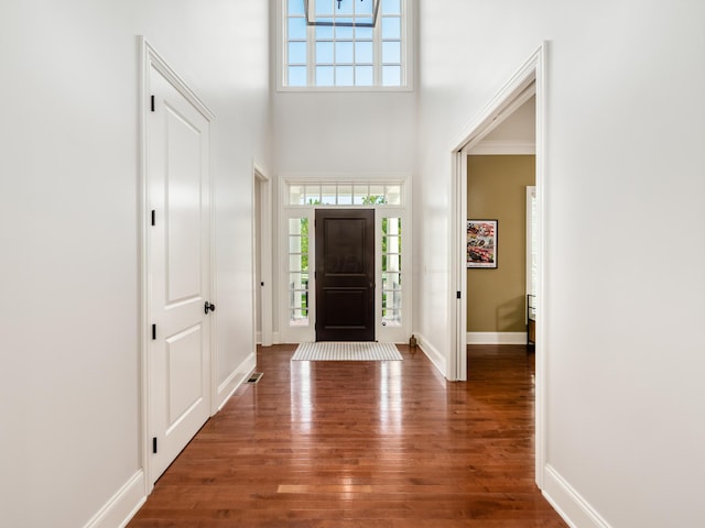 foyer entrance with dark wood-type flooring, a healthy amount of sunlight, a towering ceiling, and crown molding