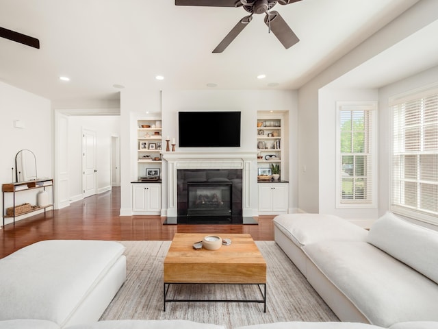 living room with a fireplace, ceiling fan, built in features, and hardwood / wood-style floors