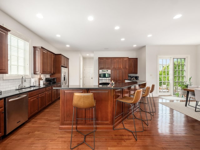 kitchen with appliances with stainless steel finishes, a kitchen island, a kitchen bar, sink, and light hardwood / wood-style flooring