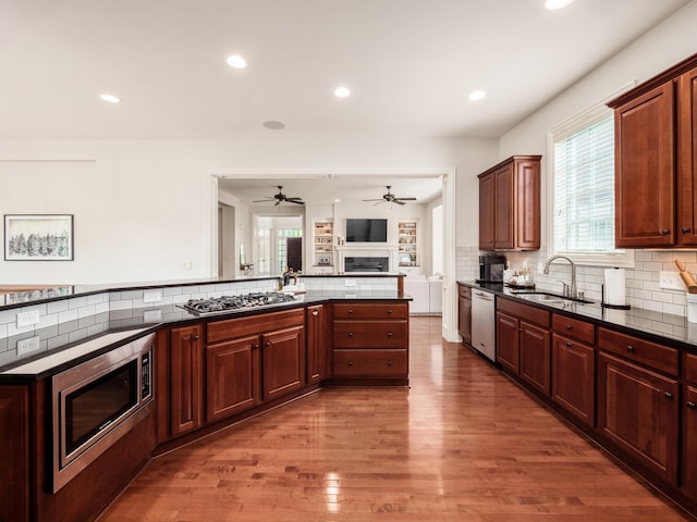 kitchen with backsplash, kitchen peninsula, sink, hardwood / wood-style flooring, and stainless steel appliances