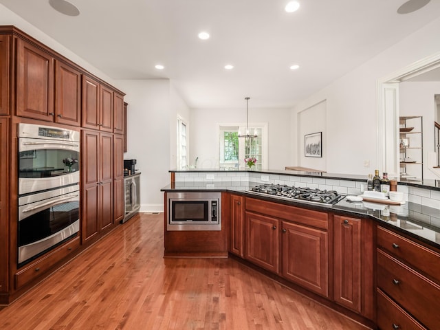 kitchen featuring pendant lighting, appliances with stainless steel finishes, tasteful backsplash, kitchen peninsula, and hardwood / wood-style flooring