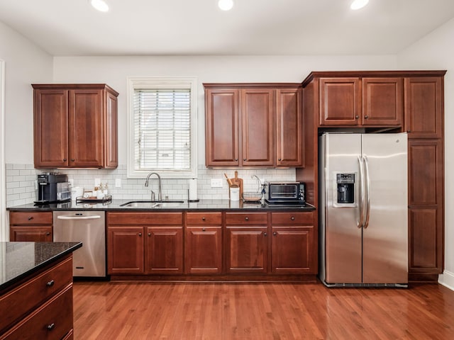 kitchen featuring tasteful backsplash, sink, light wood-type flooring, appliances with stainless steel finishes, and dark stone counters