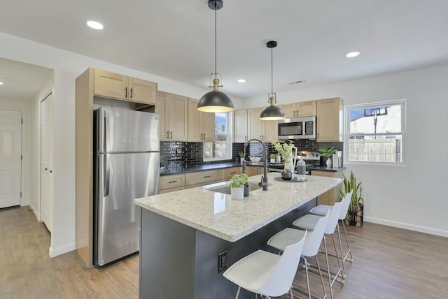 kitchen featuring light brown cabinetry, sink, appliances with stainless steel finishes, an island with sink, and light stone countertops