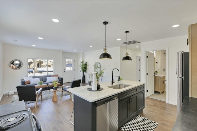 kitchen with sink, light wood-type flooring, an island with sink, pendant lighting, and stainless steel appliances