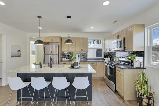 kitchen featuring pendant lighting, dark wood-type flooring, appliances with stainless steel finishes, a kitchen island, and light brown cabinetry