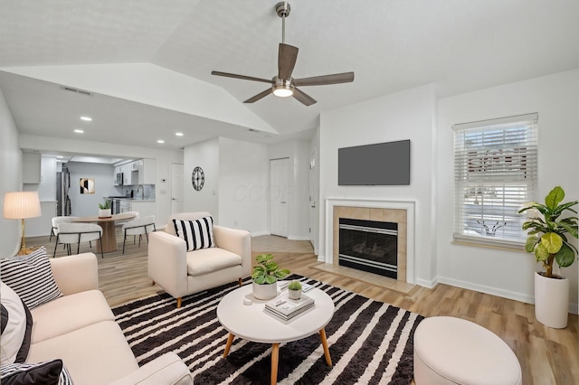 living room featuring a tiled fireplace, vaulted ceiling, light hardwood / wood-style floors, and ceiling fan