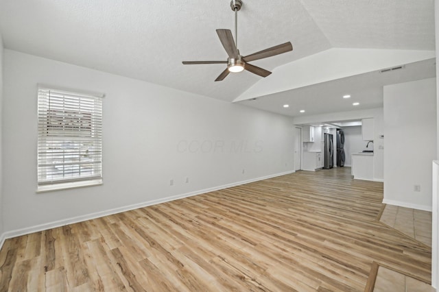 unfurnished living room with ceiling fan, lofted ceiling, light hardwood / wood-style floors, and a textured ceiling