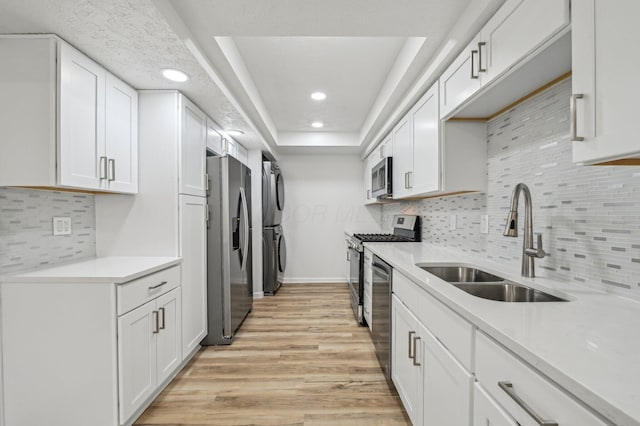 kitchen featuring stacked washer and clothes dryer, sink, light wood-type flooring, stainless steel appliances, and white cabinets