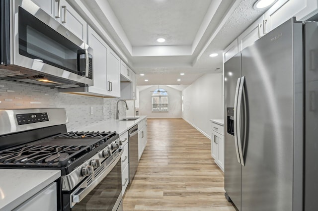 kitchen with appliances with stainless steel finishes, tasteful backsplash, white cabinetry, sink, and light wood-type flooring